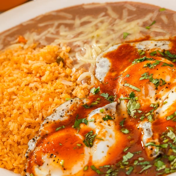 Huevos Rancheros with red sauce, cilantro, rice, and refried beans with cheese.