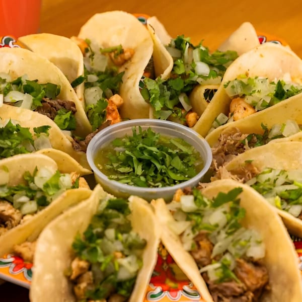 A platter of Sr. Tequila Mexican Grill tacos with various fillings, topped with cilantro and onions, and a side of green salsa.