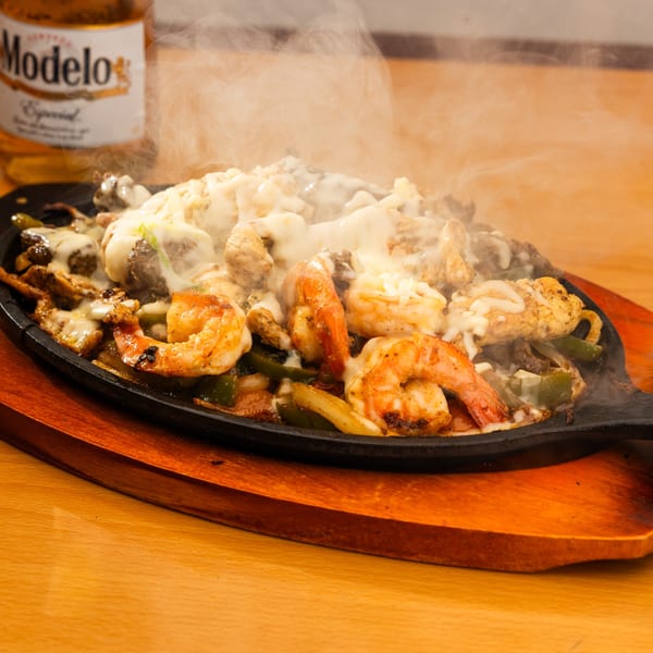 Sizzling fajitas with shrimp, chicken, and melted cheese, served with a Modelo beer.
